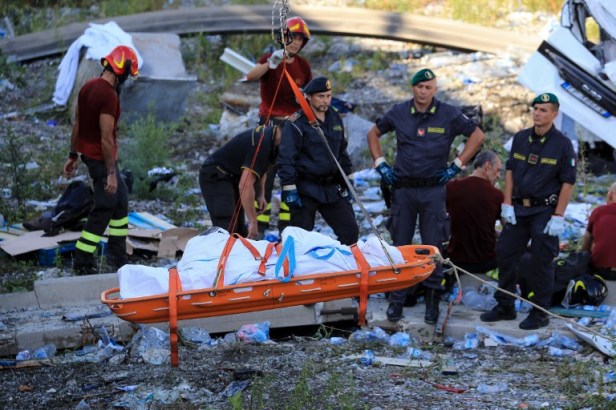 Les sauveteurs et les forces de sécurité observent comme un corps récupéré évacué sur le site où le pont de l'autoroute de Morandi s'est effondré à Gênes le 14 août 2018. Valery HACHE / AFP